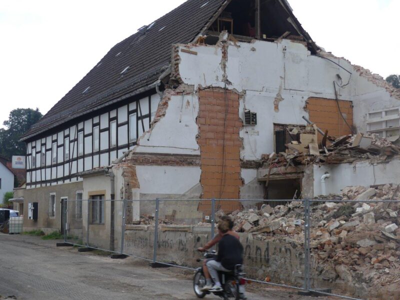 Der historische Gasthof Taubenheim mit abgerissenem Saalanbau. Im Vordergrund sind 2 Personen au einem Moped zu sehen.