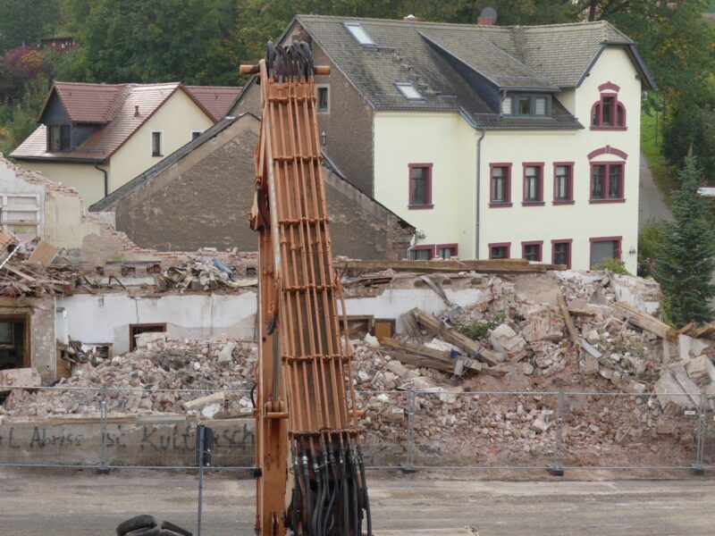 Ein Baggerarm vor einem Trümmerhaufen eines Abrisshauses